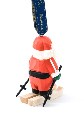 Hand-carved ski Santa ornament with red hat, black belt, skis on wooden base, hanging ribbon