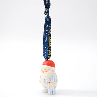 Santa ornament with red hat and blue striped pajamas; dark blue ribbon with gold script.