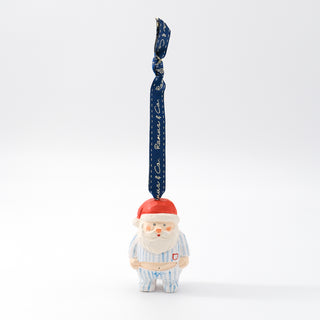Small Santa ornament standing with red hat and blue striped pajamas; looped hanging ribbon.