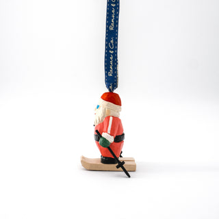 Hand-carved ski Santa ornament in profile, red suit and hat, skis and wooden base, ribbon